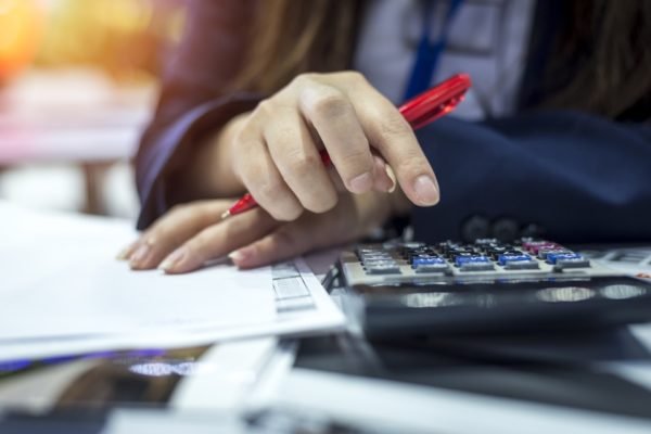 Imagem colorida de pessoa fazendo contas na calculadora, com vários papéis e contas a pagar sobre a mesa Desenrola dicas - Metrópoles