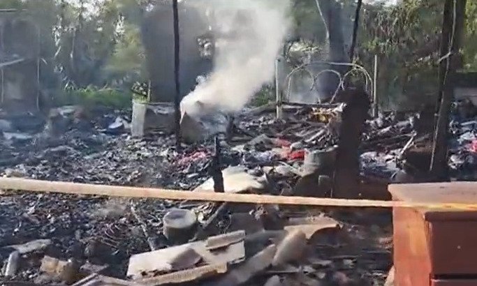 Imagem colorida de casa destruída por incêndio; fumaça sai de móveis - Metrópoles