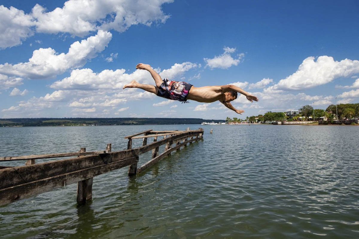 Foto colorida de homem pulando no lago - Metrópoles