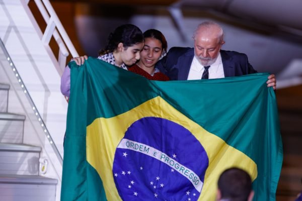 Presidente Lula com bandeira e duas jovens repatriadas após chegarem em Brasília - metrópoles
