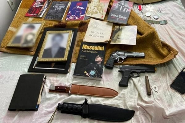 Em foto colorida duas facas, duas pistolas de brinquedo, e livros e fotos em alusão ao fascismo e nazismo sobre cama - Metrópoles