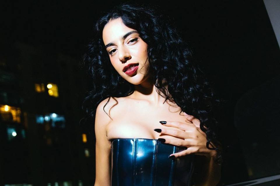 Foto colorida da cantora Marina Sena olhando para a câmera com o cabelo solto e uma blusa sem alça preta, com a mão no peito - Metrópoles