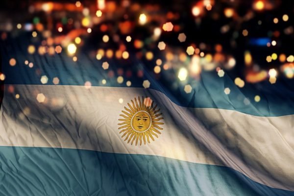 Imagem de uma bandeira da Argentina, em meio a várias luzes e com um fundo escuro - Metrópoles