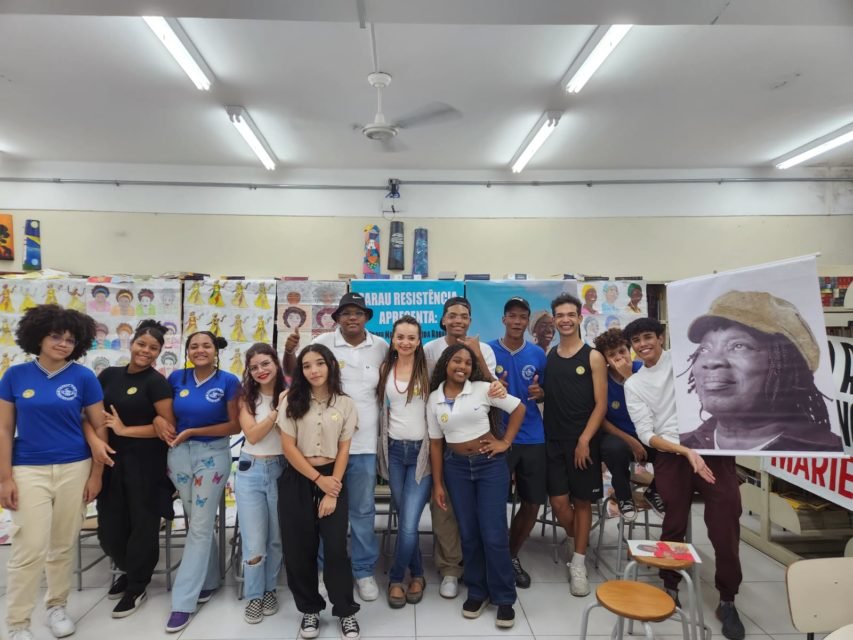 imagem colorida mostra estudantes em escola pública de são paulo. eles estão em uma biblioteca e seguram uma imagem do cantor milton nascimento - metrópoles