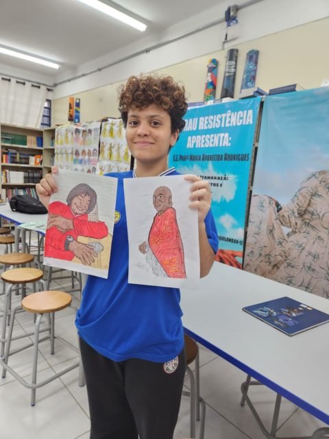 imagem colorida mostra estudante segurando dois desenhos do cantor milton nascimento - metrópoles