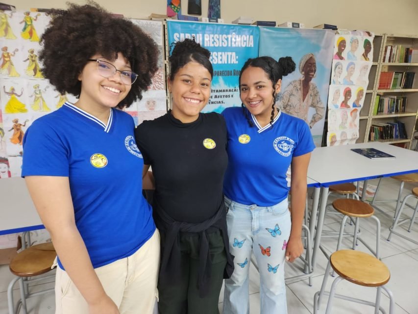 imagem colorida mostra três estudantes em biblioteca de escola. metrópoles