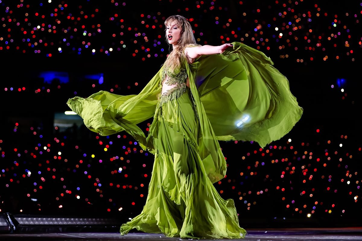 Foto de mulher loira, com vestido longo verde, rodando em um palco - Metrópoles