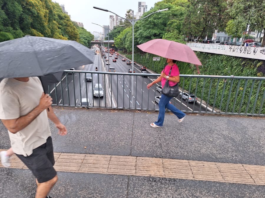 Imagem mostra pessoas com guarda-chuva sobre viaduto - Metrópoles