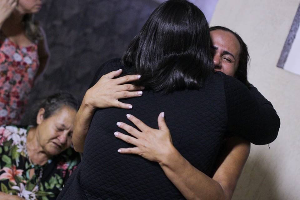 Foto colorida de mulher de roupa preta abraçando e consolando a viúva