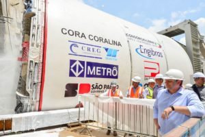 Imagem colorida mostra Tarcísio de Freitas, à direita, apoiando o braço em uma grade, vendo uma máquina tuneladora de Metrô - Metrópoles