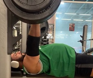 Imagem de homem com camiseta regata verde fazendo supino - Metrópoles