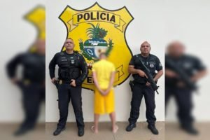 Homem com roupa amarela de costas entre dois policiais