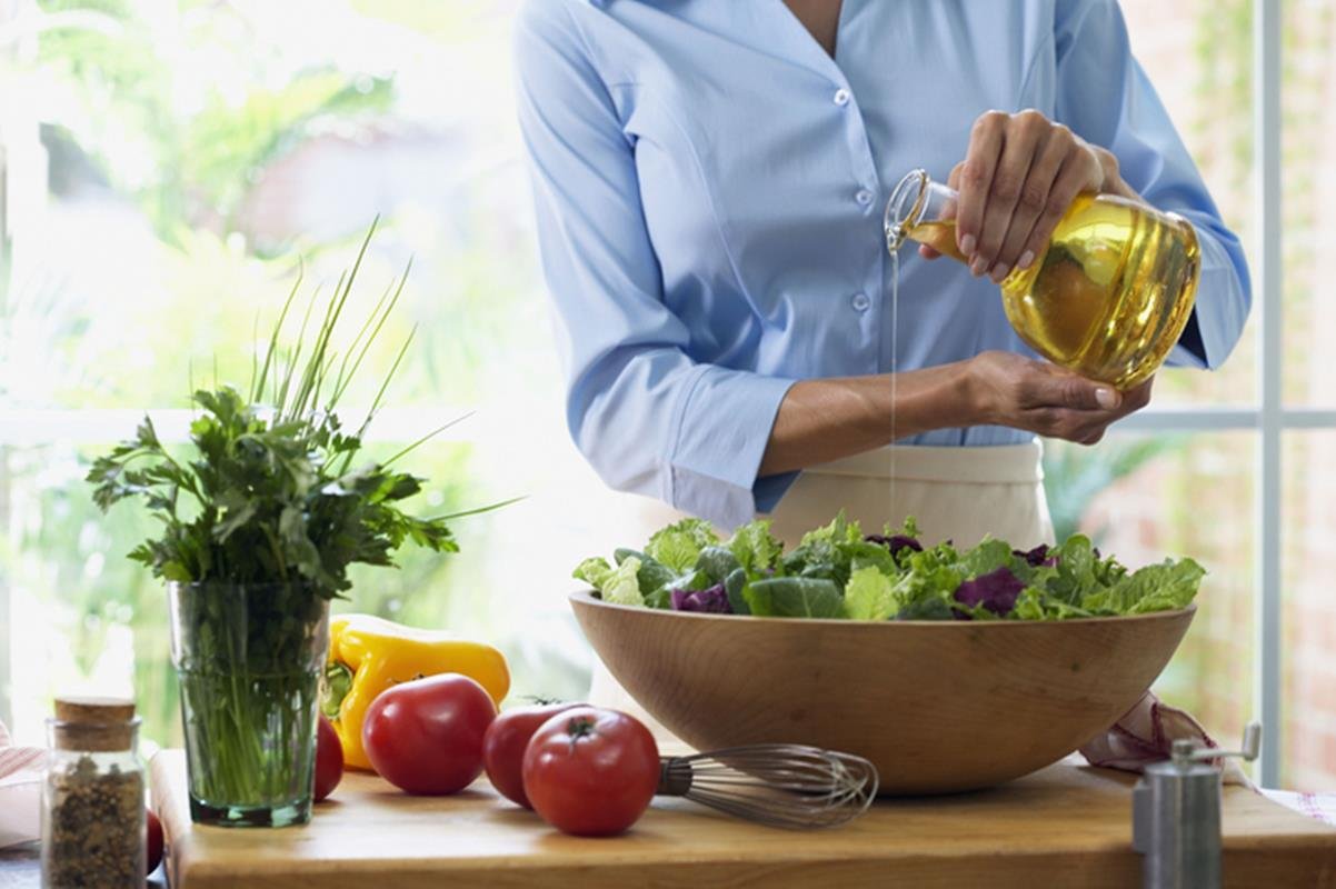 Foto de mulher colocando azeitem em salada com alface e tomate - Metrópoles