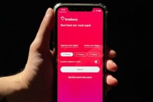 foto colorida de uma mão segurando celular; na tela, o aplicativo do banco Bradesco - Metrópoles