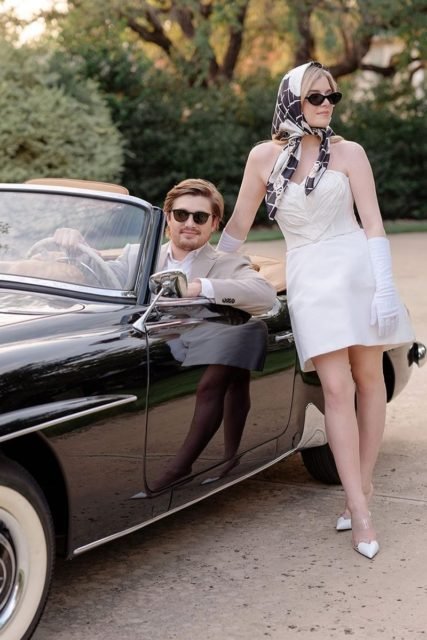 Foto colorida de homem dentro de carro antigo e de mulher em pé, escorada no automóvel - Metrópoles