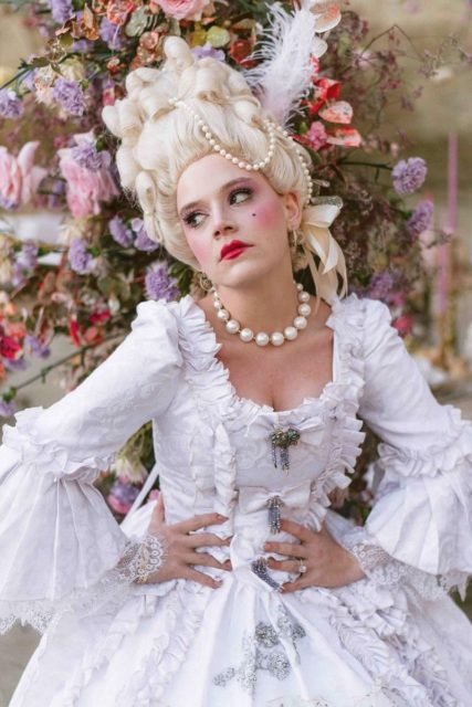 Foto colorida de mulher loira, com vestido branco e maquiagem de Maria Antonieta - Metrópoles