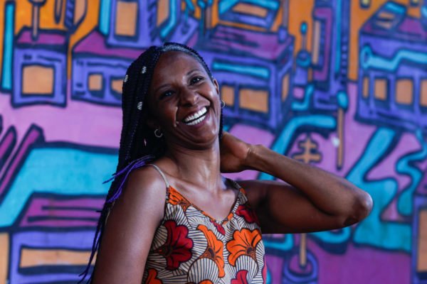 Mulher negra sorrindo com parede grafitada ao fundo
