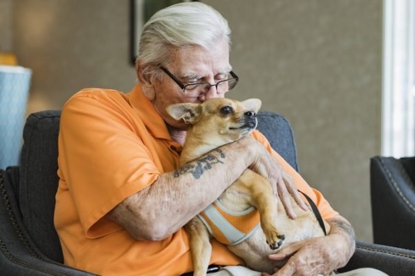 Foto de homem de cabelos brancos e camisa laranja beijando cachorro - Metrópoles