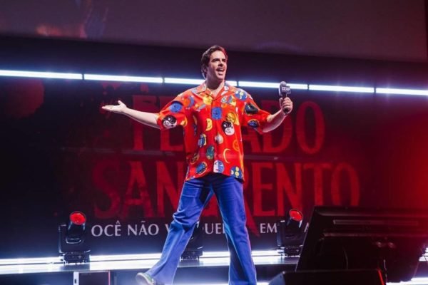 Foto colorida de Eli Roth na CCXP23, em São Paulo. Diretor aparece em cima de palco, com camisa vermelha e colorida - Metrópoles
