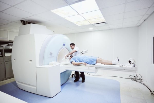 Foto colorida mostra Enfermeiro preparando paciente para ressonância magnética no hospital
