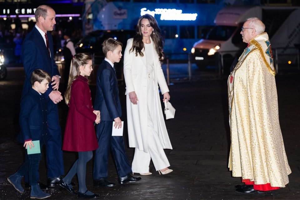 Foto de padre indo cumprimentar um casal de adultos com três crianças. O ambiente está escruro - Metrópoles