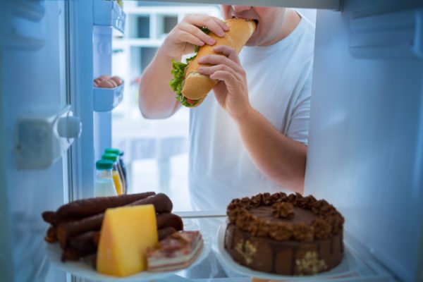 Foto mostra homem assaltando a geladeira.Homem com excesso de peso na dieta quebra dieta com sanduíche grande. Descontar na comida, estresse, excesso
