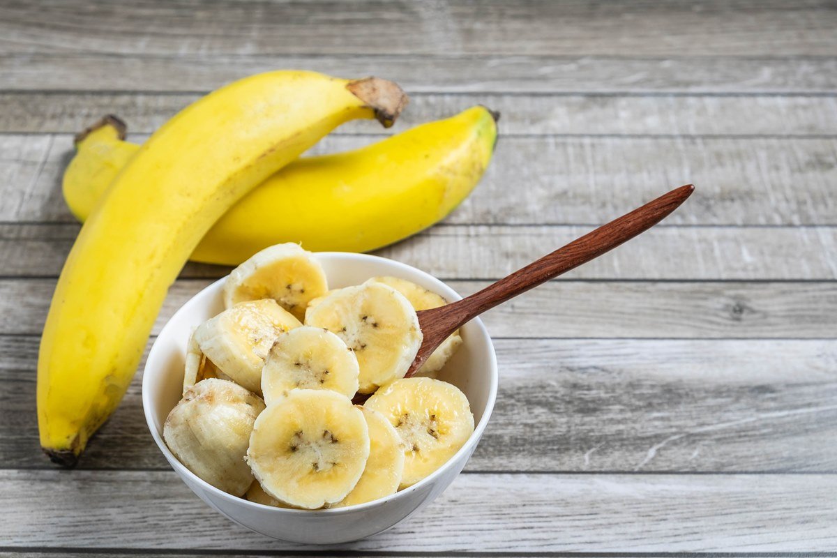 Foto colorida de duas bananas e da fruta cortada em uma tigela - Metrópoles