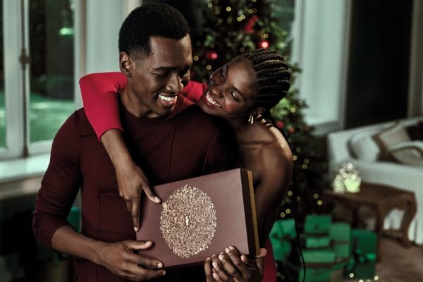 Foto colorida de um casal negro segurando uma caixa de presente do O Boticário - Metrópoles