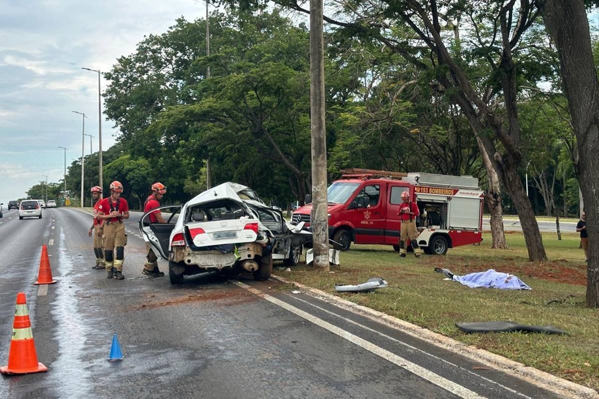 Carro branco destruído após acidente, ambulância e bombeiros do lado