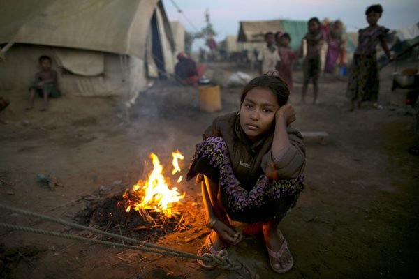 Imagem colorida de jovem sentada ao lado de fogueira, em Mianmar - Metrópoles