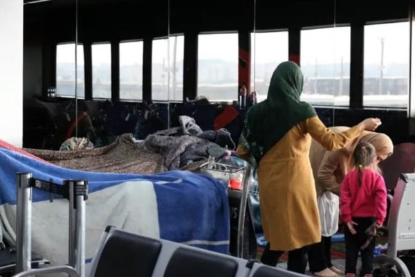 Imagem colorida mostra saguão do terminal 2 do Aeroporto Internacional de SP com cobertores formando barracas entre as cadeiras e uma mulher e uma criança caminhando no local - Metrõpoles