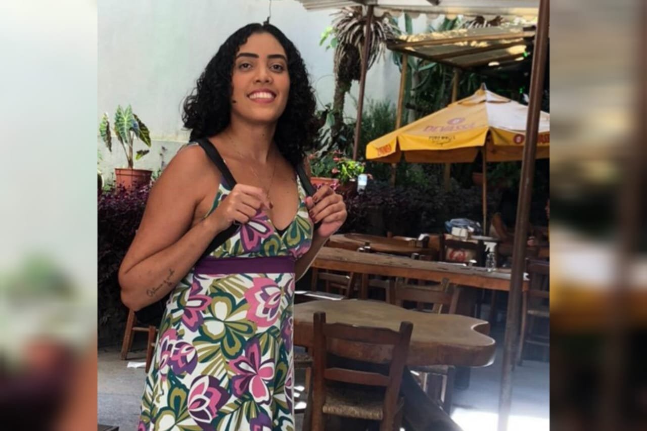 Foto mostra jovem morena de cabelos cacheados sorrindo para a câmera. É Camila, paciente que teve a doença de Crohn