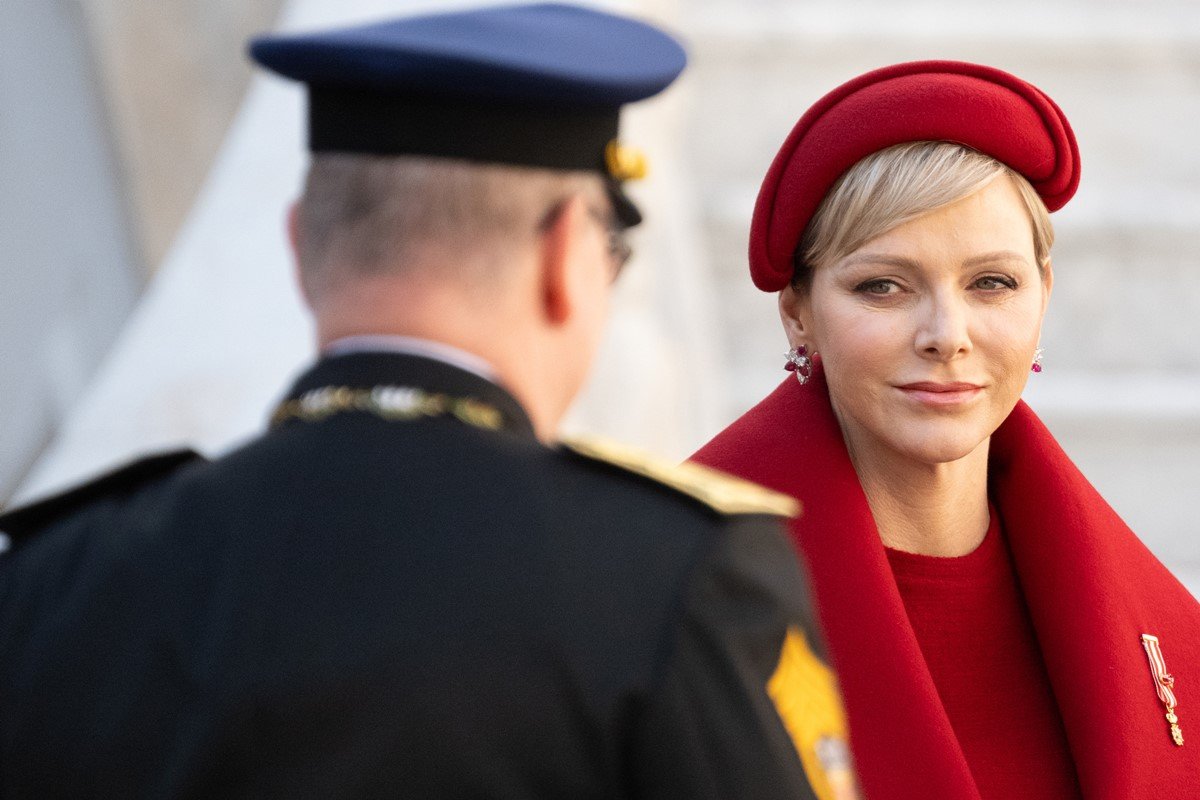 Foto de mulher com roupa vermelha olhando para homem, com trajes militares. Ele est&aacute; de costas - Metr&oacute;poles