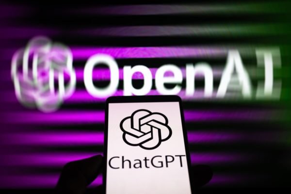 Imagem do logotipo da OpenAI, criadora do ChatGPT. À frente, em destaque, um celular com o símbolo do ChatGPT - Metrópoles