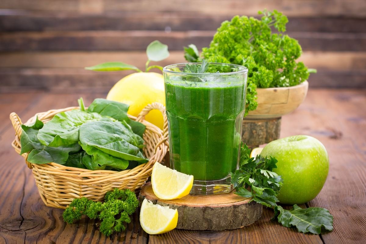 Foto de suco verde ao lado de um limão fatiado, couve, maçã verde e laranja - Metrópoles