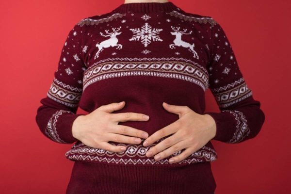 Imagem colorida de pessoa inchada com mão na barriga e roupa de Natal - Metrópoles