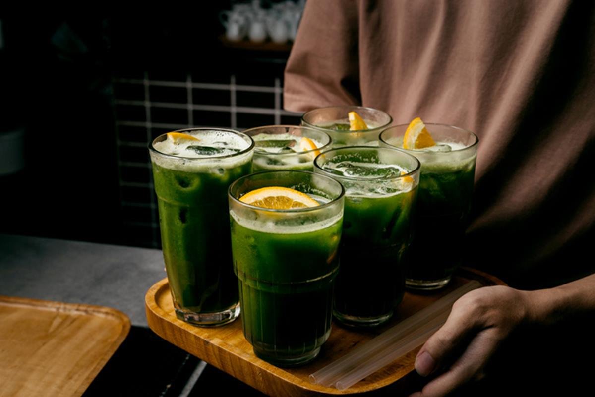 Pessoa segura bandeja com seis copos de suco verde