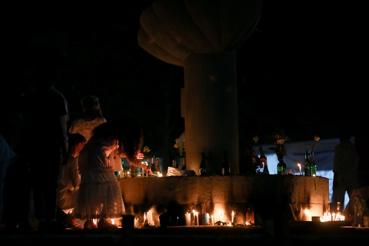 Foto de pessoas à noite acendendo velas em oferenda na prainha