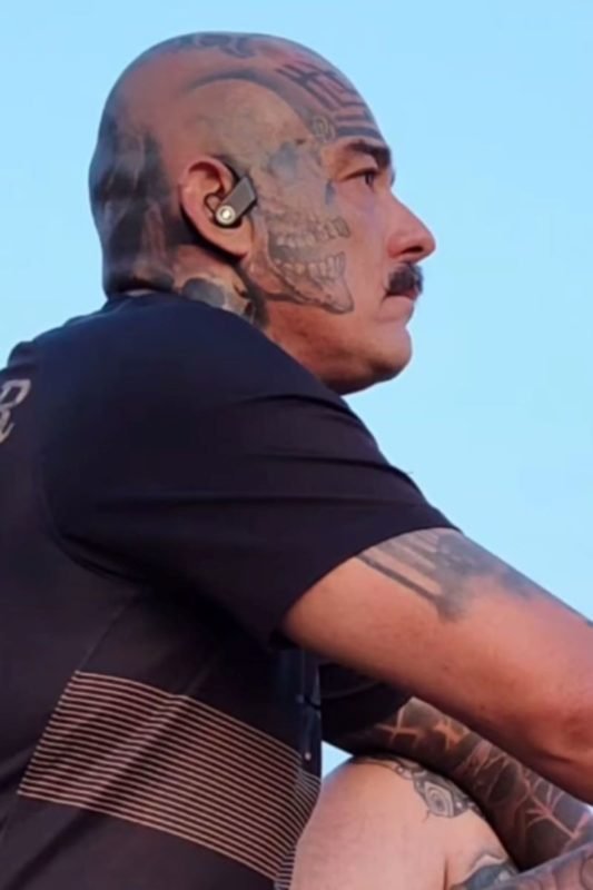 imagem colorida mostra homem com camiseta preta. ele tem tatuagens no rosto, braço e perna. metrópoles