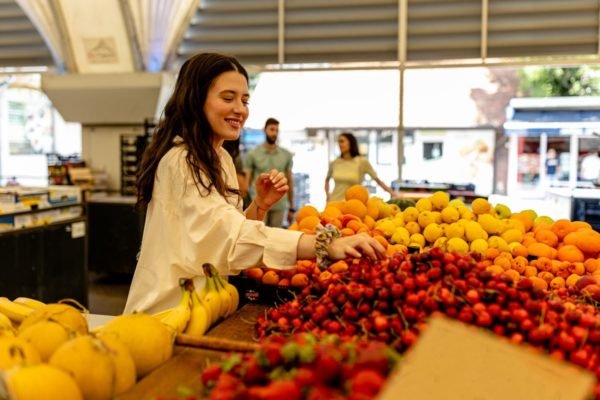 Mulher branca, de cabelos pretos e longos, compra frutas no mercado de rua - Metrópoles