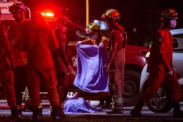 Foto colorida bombeiros cobrindo corpo de vítima atropelada no Eixão