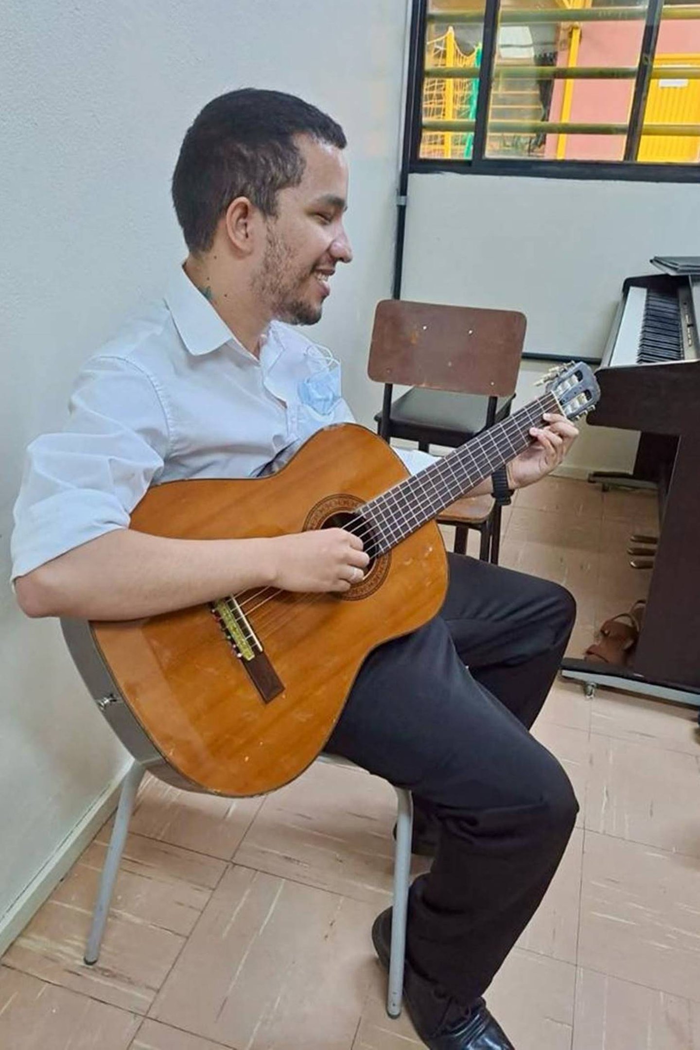 Homem de perfil tocando violão enquanto sorri - Metrópoles