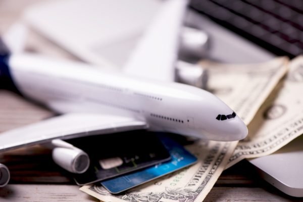 Imagem de miniatura de avião sobre cédulas de dinheiro e cartões de crédito - Metrópoles