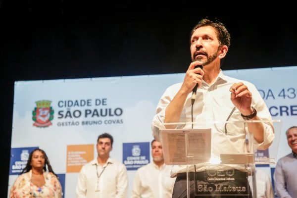 Imagem colorida mostra Ricardo Nunes falando em um púlpito transparente no palco de um evento da Prefeitura em SP - Metrópoles