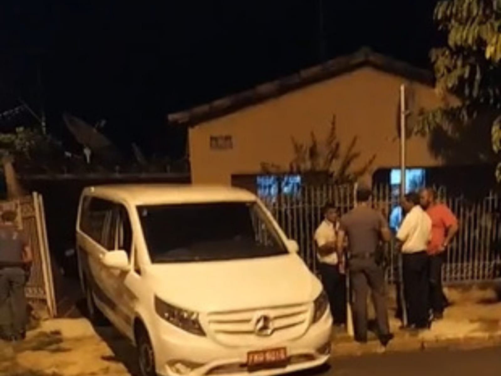 Imagem de carro funerário estacionado em frente a casa de homem que matou mulher e sogra esfaqueadas; PM e pessoas acompanham movimentação - Metrópoles