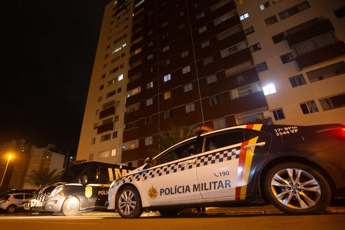 Foto de carro da polícia militar e viatura do IML em frente a prédio