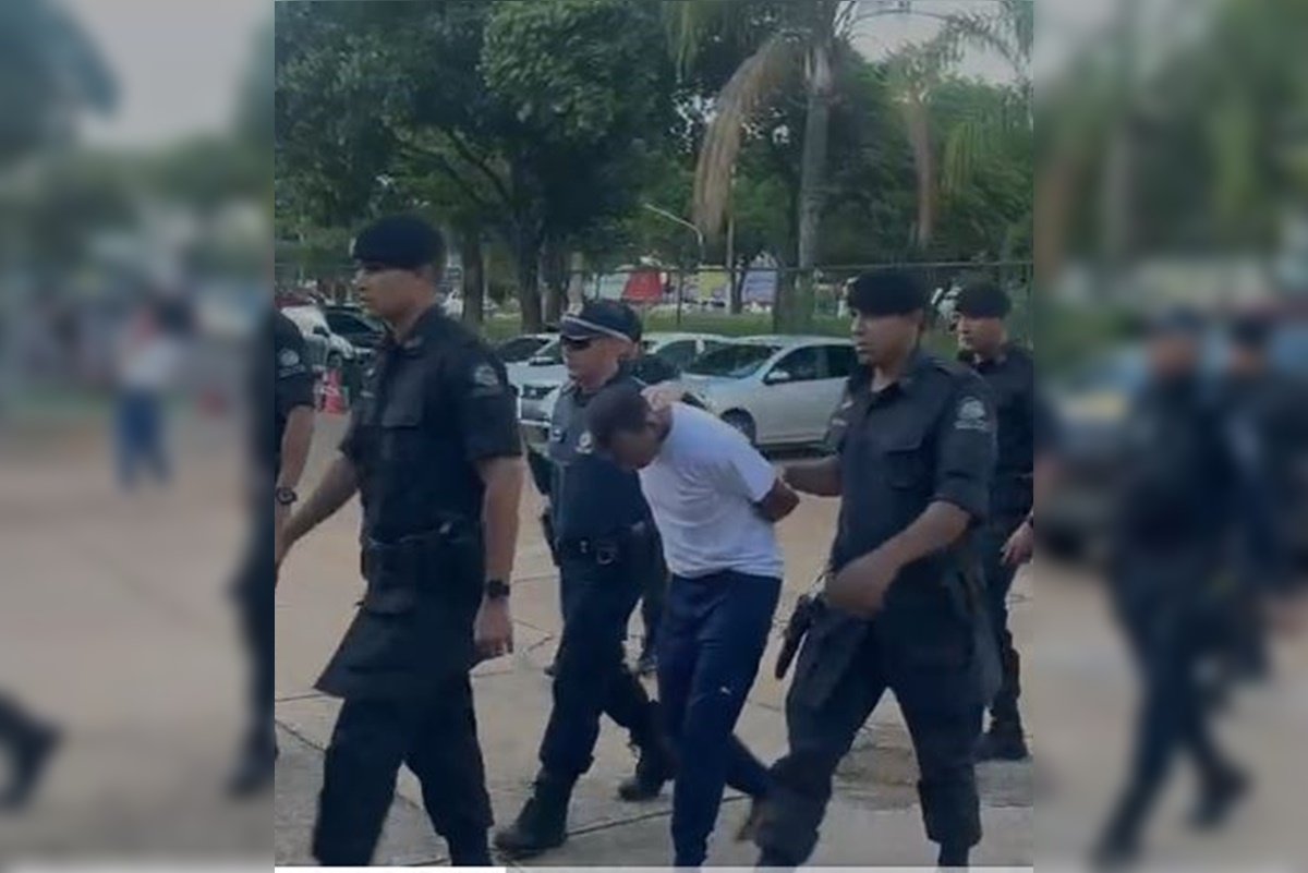 Imagem colorida de homem de camisa branca sendo preso