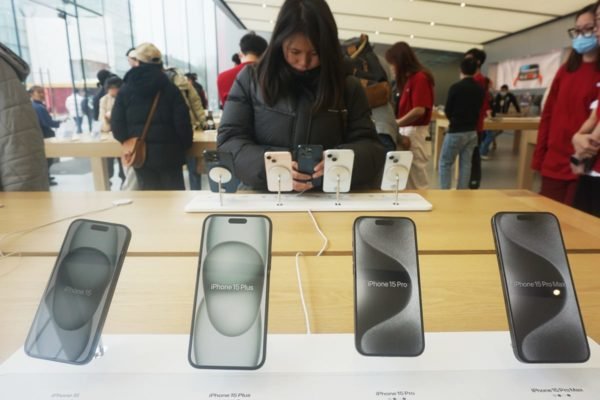 Imagem de loja da Apple, com inúmeros iPhones à venda, e consumidora mexendo em um deles - Metrópoles