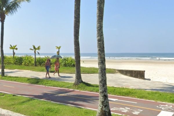 Foto mostra jardim da praia no bairro Jardim Real, em Praia Grande, com dois turistas andando na calçada - Metrópoles