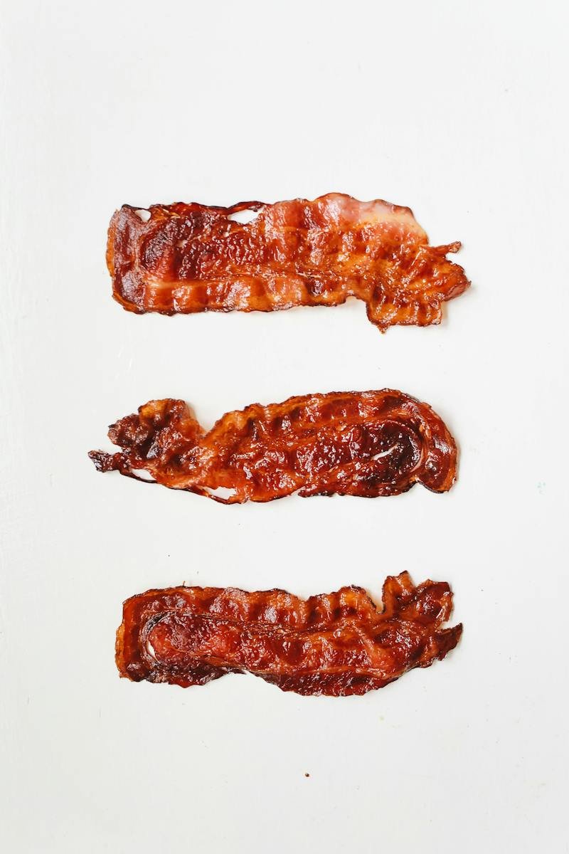Três fatias de bacon em fundo branco - Metrópoles